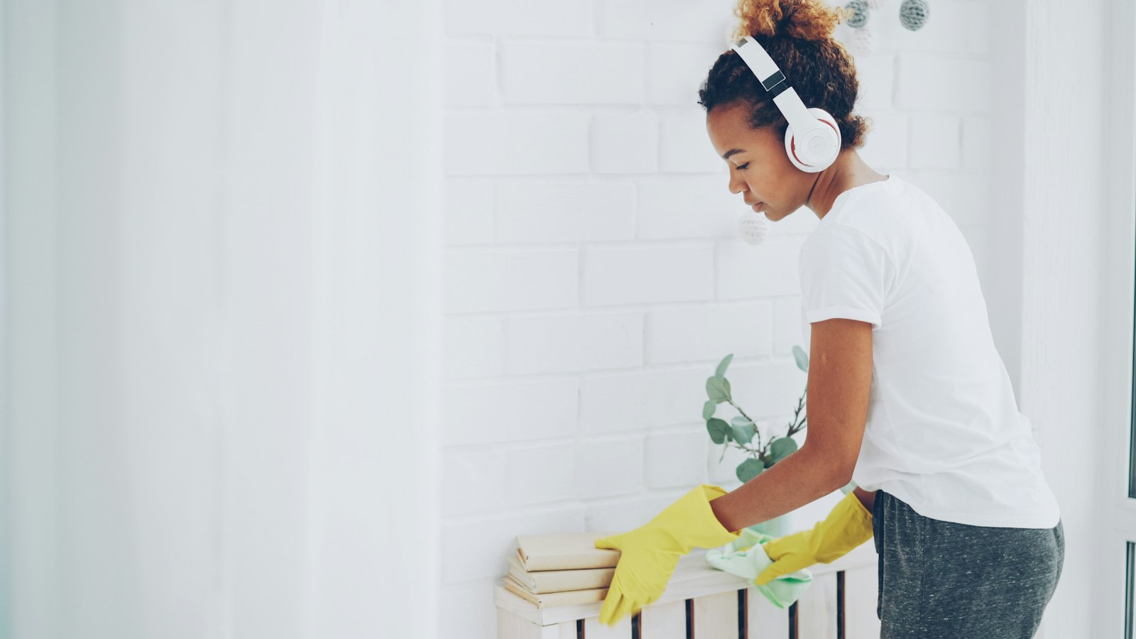 Woman wearing rubber gloves wiping and cleaning a white shelf at home
