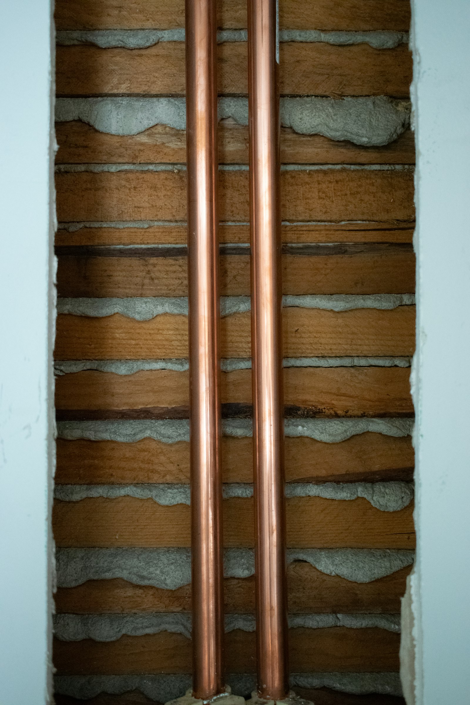 Two copper refrigeration pipes running vertically along a wall