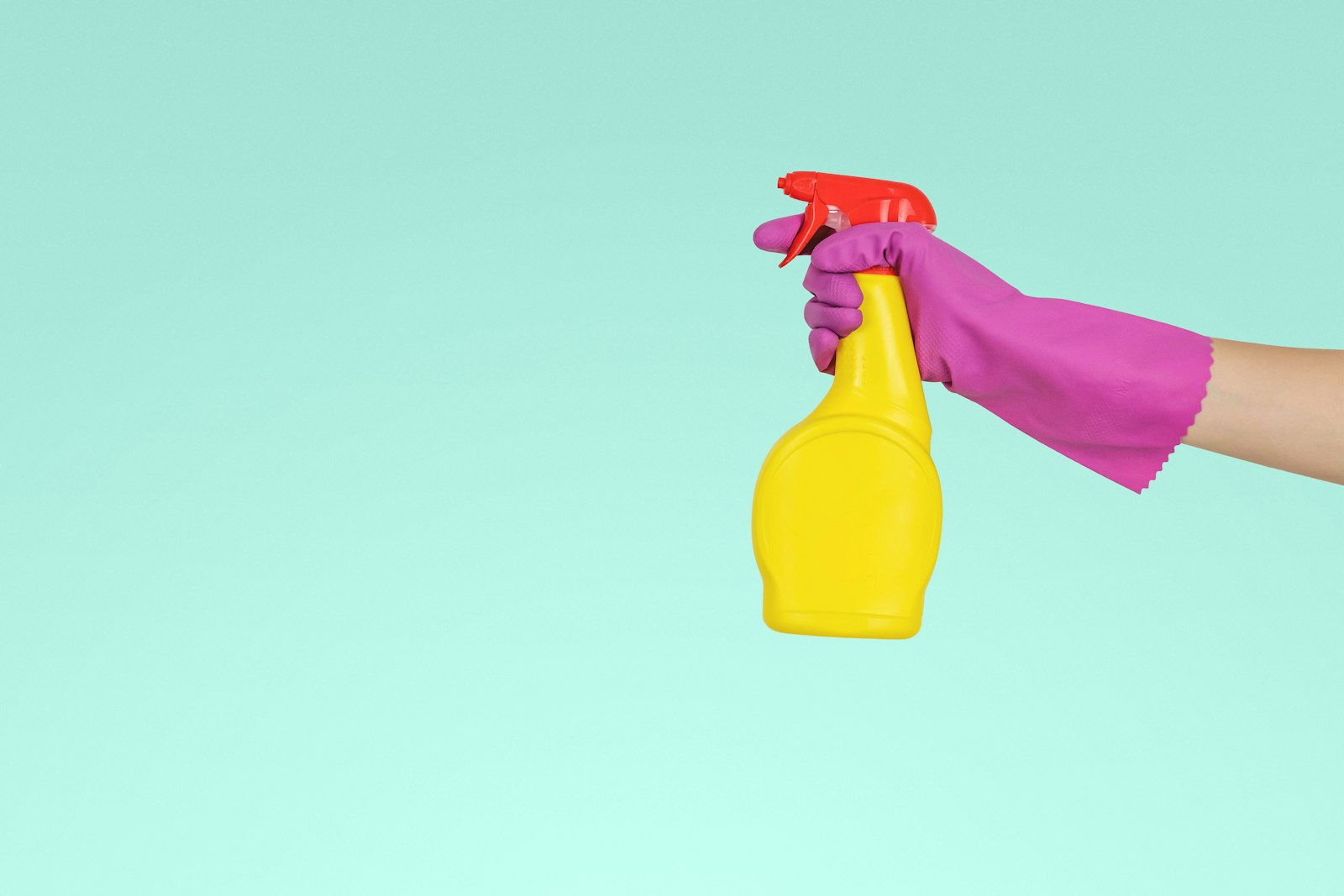 Gloved hand holding a yellow spray bottle against a turquoise background