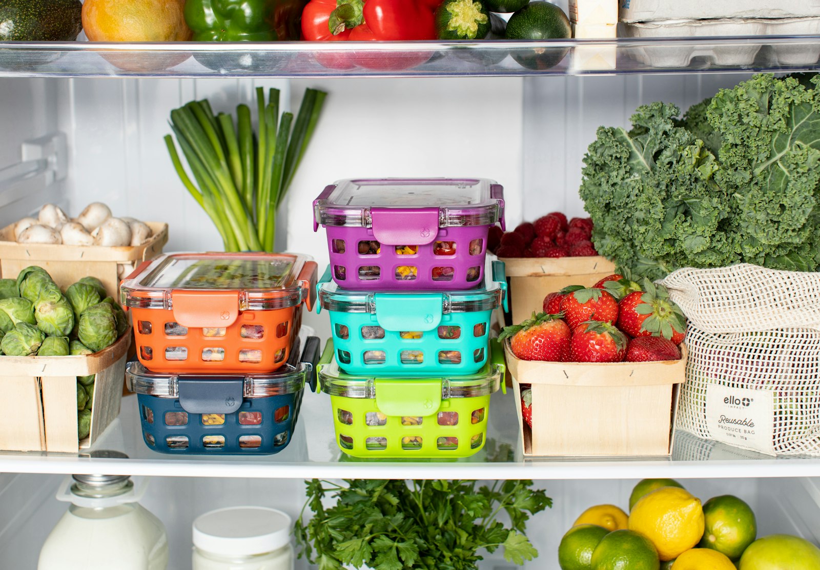Colourful food storage containers and fresh vegetables neatly arranged inside a clean refrigerator